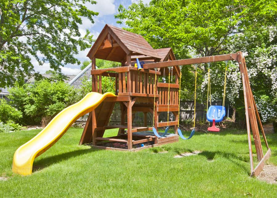 Back Yard Wooden Swing Set On Green Lawn