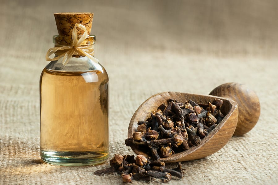 Close Up Glass Bottle Of Clove Oil And Cloves In Wooden Shovel On Burlap Sack