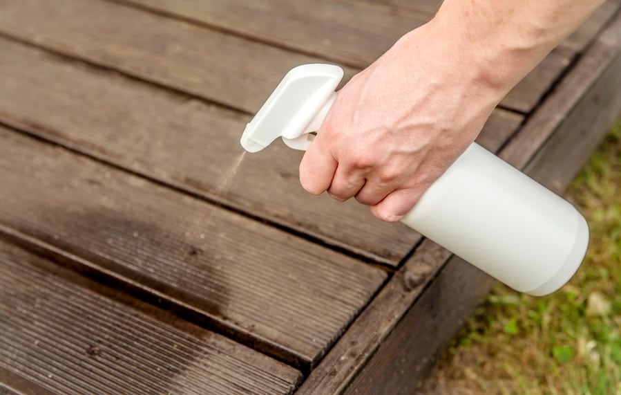 Person Hand Spraying Insect Repellent On Home Terrace Wood Boards.