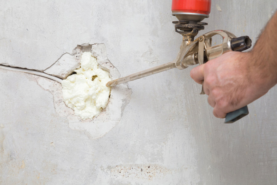 Young Man Hand Using Spray Gun And Filling Hole With Construction Foam In Concrete Wall Where Was Old Outlet