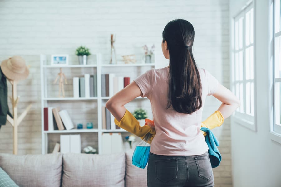 Young Wife Finished House Chores Putting Hands In Waist Watching The Bookshelf Beside The Sunlight Window