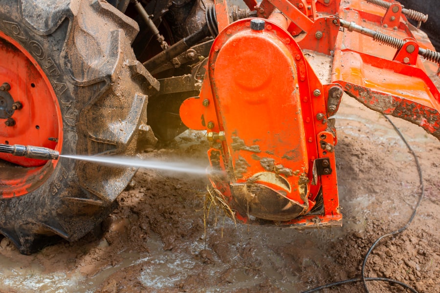 Farmers Using High Pressure Washer To Clean A Tractor