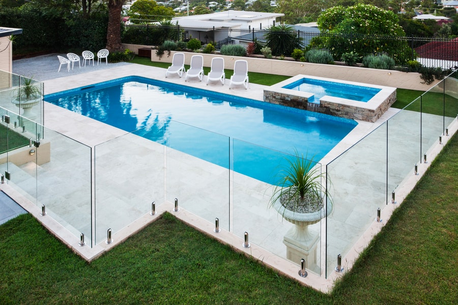 Modern Swimming Pool Covered With Glass Panels Beside A Green Lawn Garden Including Trees And Chairs