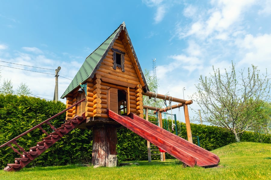 Small Wood Log Playhouse Hut With Stairs Ladder And Wooden Slide On Children Playground At Park Or House Yard.