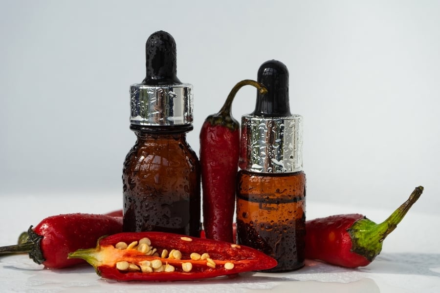 Glass Bottle Of Essential Oil With Fresh Red Chili Pepper On A White Background.