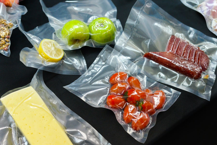 Vacuum Sealed Vegetables, Tomato, Cheese, Meat, Lemon, Apple On A Black Background Top View, Ready To Be Cooked